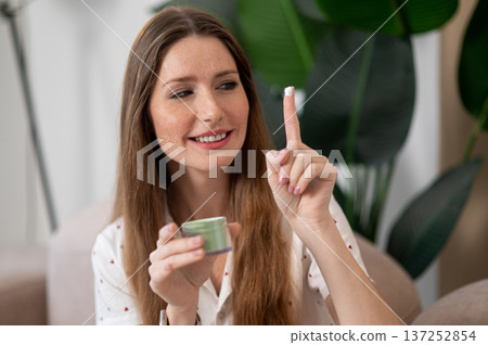 Pretty woman using face cream and looking excited Pretty woman using face cream and looking excited 137252854