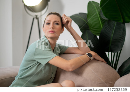Young woman sitting on the sofa and looking thoughtful Young woman sitting on the sofa and looking thoughtful 137252869