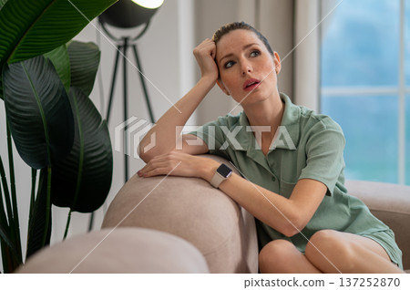 Young woman sitting on the sofa and looking thoughtful 137252870