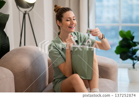 Smiling woman opening a paper bag and taking out face cream Smiling woman opening a paper bag and taking out face cream 137252874
