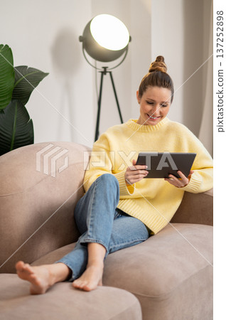 Young woman with tablet in hands lying on the sofa 137252898