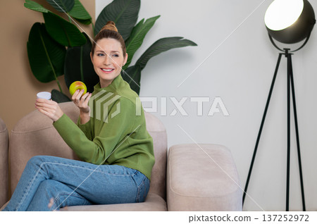 Young smiling woman in green with apple in hand Young smiling woman in green with apple in hand 137252972