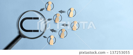 Top view of wooden figures being drawn by a magnet icon through a magnifying glass on a light blue background. Illustrates lead generation, HR recruitment, and client acquisition concepts 137253055
