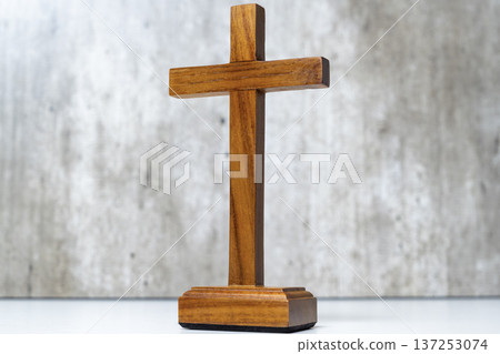 A polished wooden Christian cross on a rectangular base, standing centered against a light grey textured background. This minimalist religious symbol captures a sense of faith, peace, and spiritual A polished wooden Christian cross on a rectangular base, standing centered against a light grey textured background. This minimalist religious symbol captures a sense of faith, peace, and spiritual 137253074
