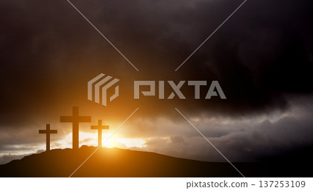Silhouette of three wooden crosses standing on a hilltop under a dark, stormy, and dramatic sky with golden sunlight breaking through the clouds. Symbolic of Calvary, Easter, and religious faith 137253109