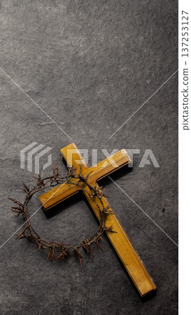 A wooden cross with a crown of thorns resting on it, set against a dark textured slate background. Symbolic of Jesus Christ's sacrifice, Good Friday, and Easter A wooden cross with a crown of thorns resting on it, set against a dark textured slate background. Symbolic of Jesus Christ's sacrifice, Good Friday, and Easter 137253127