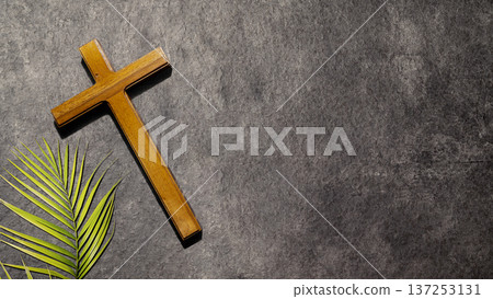 A wooden cross and a green palm frond on a textured dark gray stone surface with copy space. Conceptual image for Palm Sunday, Lent, Holy Week, and Easter religious celebrations A wooden cross and a green palm frond on a textured dark gray stone surface with copy space. Conceptual image for Palm Sunday, Lent, Holy Week, and Easter religious celebrations 137253131