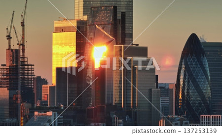 United Kingdom, London: Warm sunlight reflecting in modern glass skyscrapers in London financial district at sunset, construction cranes in the background, development and growth. Aerial view United Kingdom, London: Warm sunlight reflecting in modern glass skyscrapers in London financial district at sunset, construction cranes in the background, development and growth. Aerial view 137253139