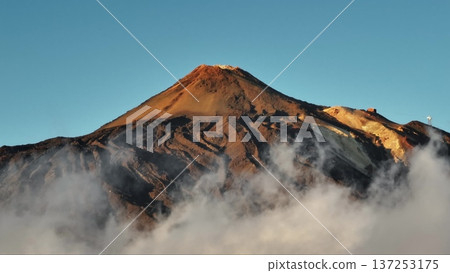 Tenerife, Canary Islands: Low clouds covering Mount Teide's slopes create a breathtaking sunrise scene. Towering peak of a volcano against clear blue sky, stunning landscape. Static shot 137253175
