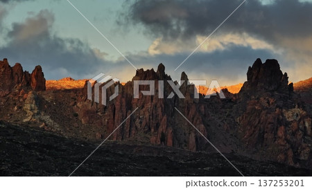 Tenerife, Canary Islands: Mountain rise dramatically against colorful sunset sky. Rugged peaks of Mount Teide with warm hues, casting long shadows across Tenerife's volcanic landscape. Drone 137253201