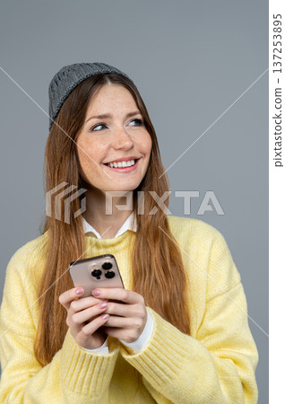 Cute young woman with a phone in hand on a grey background Cute young woman with a phone in hand on a grey background 137253895