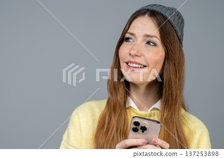 Cute young woman with a phone in hand on a grey background Cute young woman with a phone in hand on a grey background 137253898