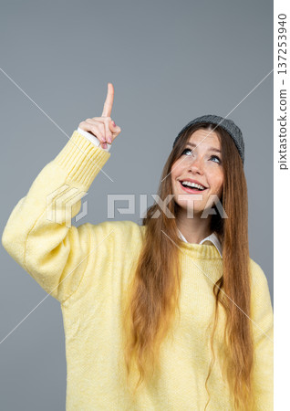 Young woman in yellow sweater pointing up with her finger Young woman in yellow sweater pointing up with her finger 137253940