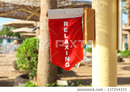 A warning flag under an umbrella on the beach with the inscription We are relaxing, do not disturb A warning flag under an umbrella on the beach with the inscription We are relaxing, do not disturb 137254335