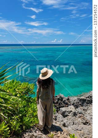 Back view of a woman looking out at the turquoise sea from a rocky spot in Okinawa Back view of a woman looking out at the turquoise sea from a rocky spot in Okinawa 137254572