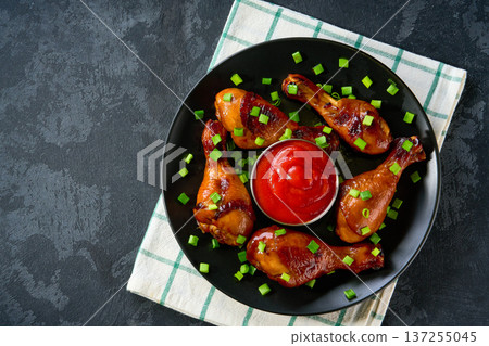 Fried chicken legs with sauce on a black table, top view. Roast chicken drumsticks with ketchup. Fried chicken legs with sauce on a black table, top view. Roast chicken drumsticks with ketchup. 137255045