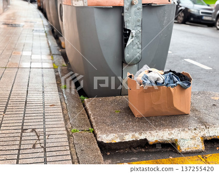 Cardboard box with clothing on sidewalk near street containers Cardboard box with clothing on sidewalk near street containers 137255420