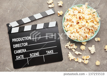 A clapper and a bucket of delicious salted popcorn on grey concrete background. A clapper and a bucket of delicious salted popcorn on grey concrete background. 137255510