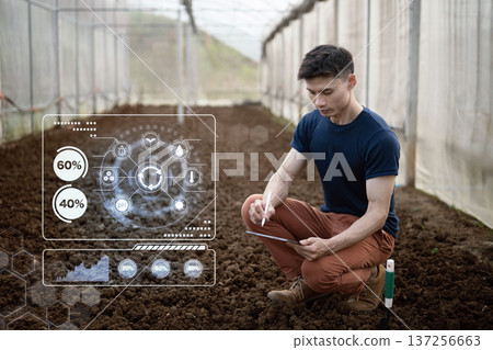 Farmer analyzes soil conditions in greenhouse using tablet and digital data interface to monitor nutrients moisture and crop readiness. 137256663