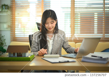 Real estate professional calculating property costs at desk, businesswoman calculating housing expenses. 137256707