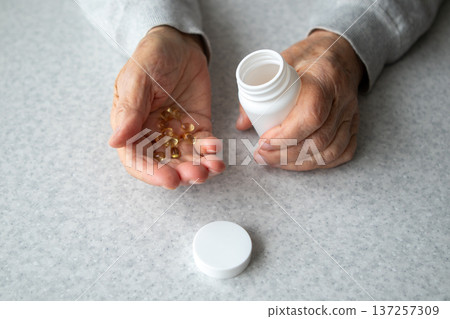 Elderly hands holding vitamin capsules with pill bottle on kitchen table for senior health 137257309