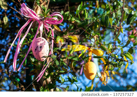 Pink Easter egg decoration with ribbon hanging on leafy tree branches in spring sunlight Pink Easter egg decoration with ribbon hanging on leafy tree branches in spring sunlight 137257327