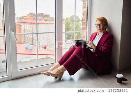 Female journalist with crimson hair views street from window Female journalist with crimson hair views street from window 137258221