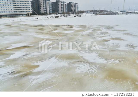 Cold city shoreline scene. Snowy waterfront with thin ice patches Cold city shoreline scene. Snowy waterfront with thin ice patches 137258225