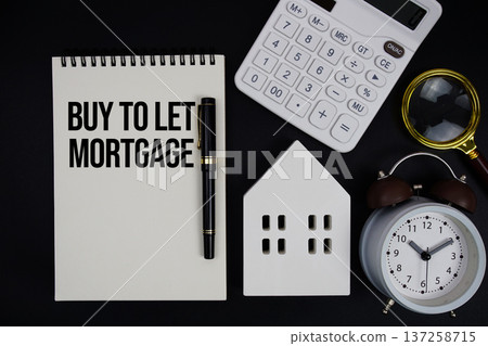 Notepad with the phrase "Buy To Let Mortgage" surrounded by a pen, calculator, magnifying glass, clock, and house model 137258715