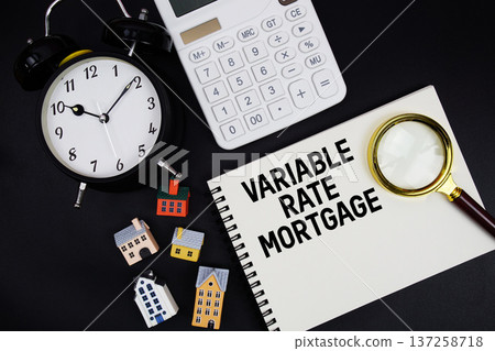 Notepad with the phrase "Variable Rate Mortgage" surrounded by a pen, calculator, magnifying glass, clock, and house model Notepad with the phrase "Variable Rate Mortgage" surrounded by a pen, calculator, magnifying glass, clock, and house model 137258718