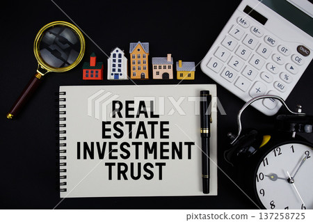 Notepad with the phrase "Real Estate Investment Trust" surrounded by a pen, calculator, magnifying glass, clock, and house model Notepad with the phrase "Real Estate Investment Trust" surrounded by a pen, calculator, magnifying glass, clock, and house model 137258725