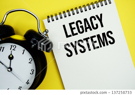 Legacy Systems text with alarm clock flat lay on yellow background 137258733