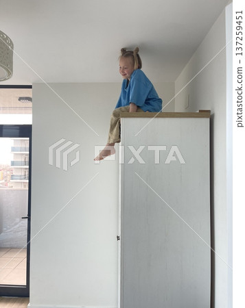 Small kid girl sitting on a high cabinet. Child 6 years old at home 137259451