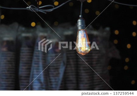 Vintage Edison light bulb glowing against a dark background with golden bokeh lights in the distance. Vintage Edison light bulb glowing against a dark background with golden bokeh lights in the distance. 137259544