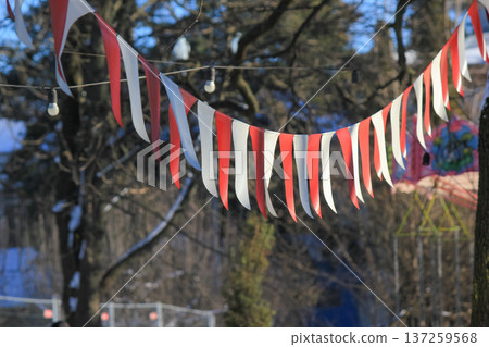 Red and white festive bunting flags hanging on a string in a sunny park during a winter celebration. 137259568