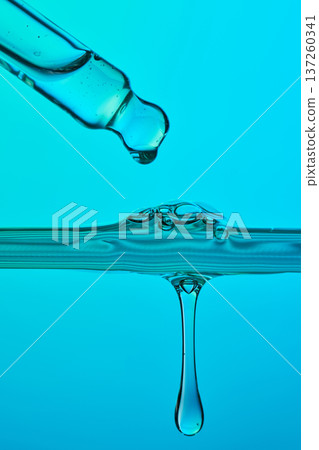 Dropper dispensing blue serum liquid into water 137260341