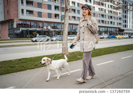 Young woman walking pet dog on urban street Young woman walking pet dog on urban street 137260789