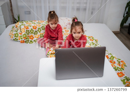 Little twin girls watching laptop on bed at home 137260799