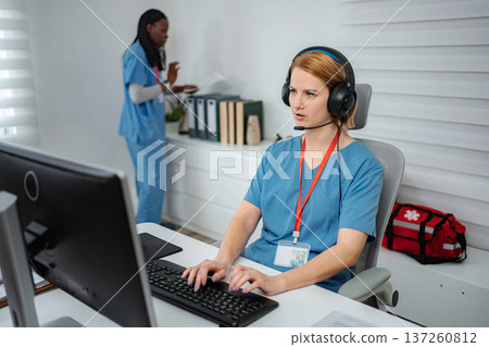 Healthcare employee talking on headset at computer Healthcare employee talking on headset at computer 137260812