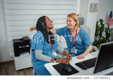 Diverse nurses laughing enjoying camaraderie at office desk Diverse nurses laughing enjoying camaraderie at office desk 137260821