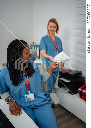 Nurses cooperating in hospital office passing documents to each other Nurses cooperating in hospital office passing documents to each other 137260827