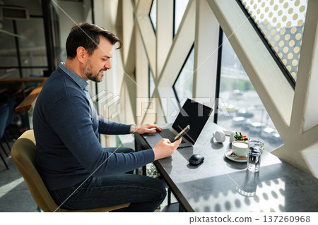 Mature adult man working on laptop and smartphone Mature adult man working on laptop and smartphone 137260968
