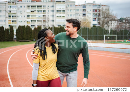 Diverse couple smiling, embracing on running track after workout 137260972
