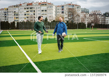 Two men walking and talking on soccer field 137260974