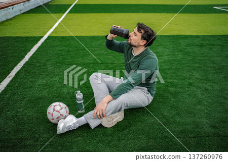 Male soccer player drinking water on green field Male soccer player drinking water on green field 137260976