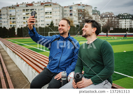 Adult men friends sitting on stadium bench taking selfie enjoying sport 137261313