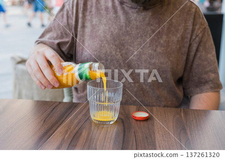 Orange juice pouring into glass at outdoor cafe table in city environment. Refreshment ritual, thirst satisfaction, beverage enjoyment, and everyday lifestyle moment during urban leisure break 137261320
