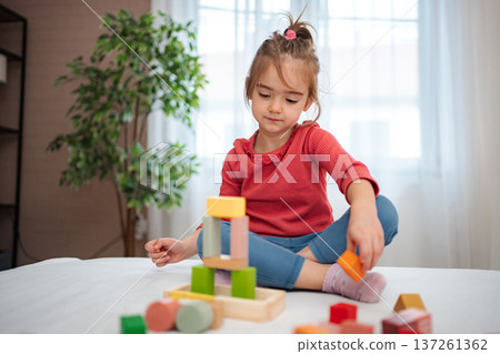 Little girl playing with colorful wooden building blocks at home 137261362