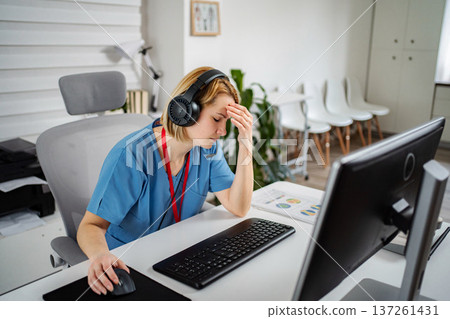 Tired nurse wearing headphones working on computer in office 137261431