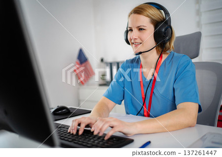 Nurse wearing headset typing on computer for telehealth consultation 137261447
